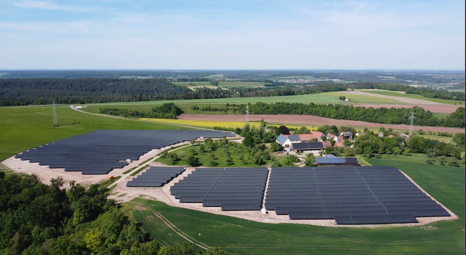 Luftaufnahme eines Solarparks bei Ansbach: mehrere Modulfelder neben einem Hof, umgeben von Wiesen und Wald