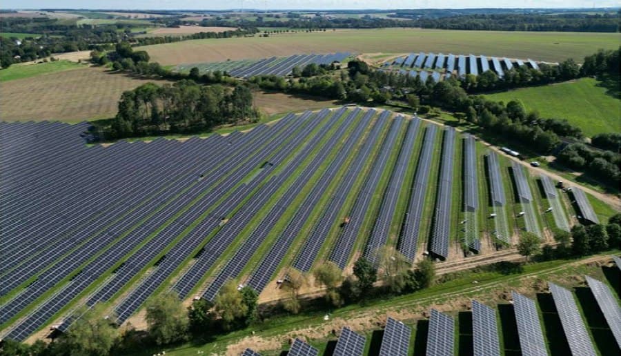 Luftaufnahme des Solarparks bei Freiberg mit geschwungenen Modulreihen zwischen Feldern und Baumreihen