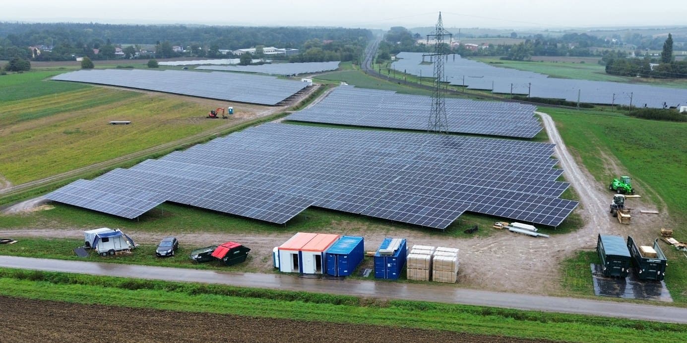 Luftaufnahme des neu errichteten Solarparks bei Kitzingen mit Baucontainern am Feldweg, darüber eine Hochspannungsleitung