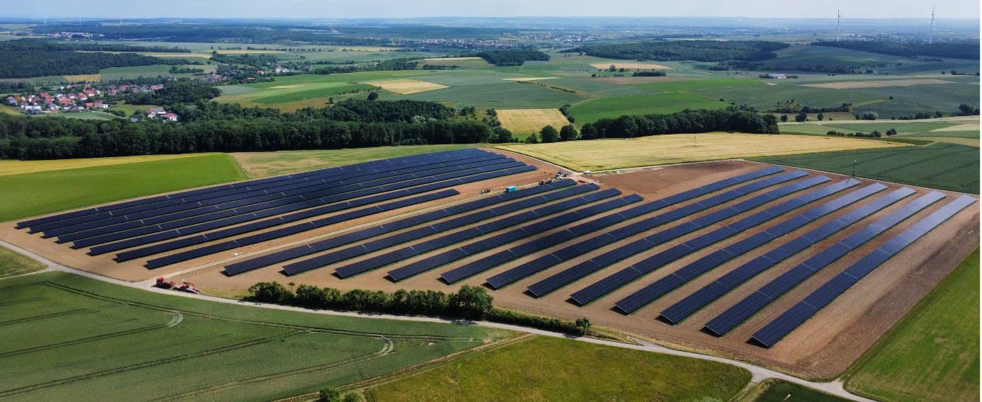 Luftaufnahme eines Solarparks bei Schweinfurt mit langen Modulreihen auf einem Feld, im Hintergrund ein Dorf