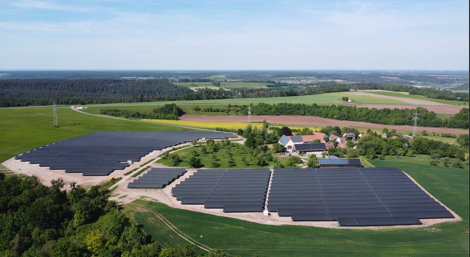 Luftaufnahme eines Solarparks bei Ansbach: mehrere Modulfelder neben einem Hof, umgeben von Wiesen und Wald