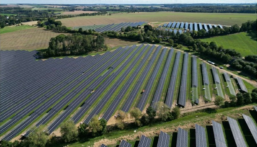 Luftaufnahme des Solarparks bei Freiberg mit geschwungenen Modulreihen zwischen Feldern und Baumreihen